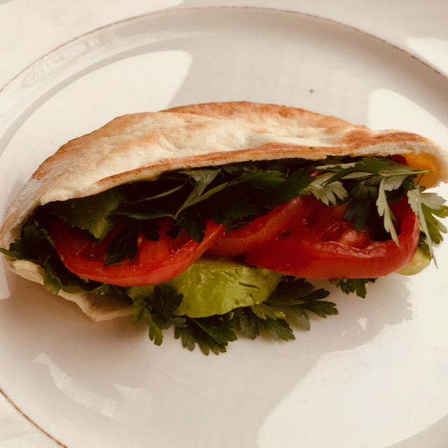 Gluten free pita sandwich on a white plate. The pita is stuffed with parsley, tomato and avocado