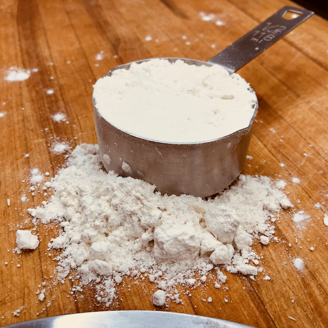 Image of a ½ cup metal measuring cup full of Make It GF gluten free flour. a small pile of flour is in front of the filled measuring cup